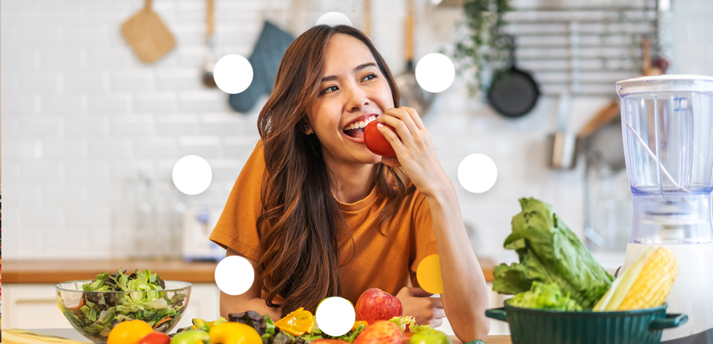 imagem de uma jovem segurando uma fruta em frente uma bancada repleta de frutas e legumes. Simbolizando Dicas essenciais para aproveitar as festas de fim de ano com bem-estar.