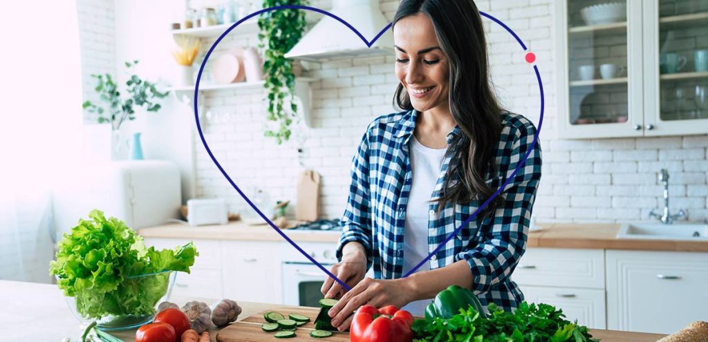 imagem de uma mulher em frente de uma bancada cortando alguns alimentos, simbolizando Como melhorar seu intestino com escolhas alimentares saudáveis